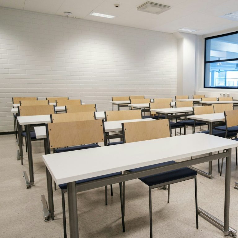 Salle de classe avec des rangées de bureaux et des chaises vides.