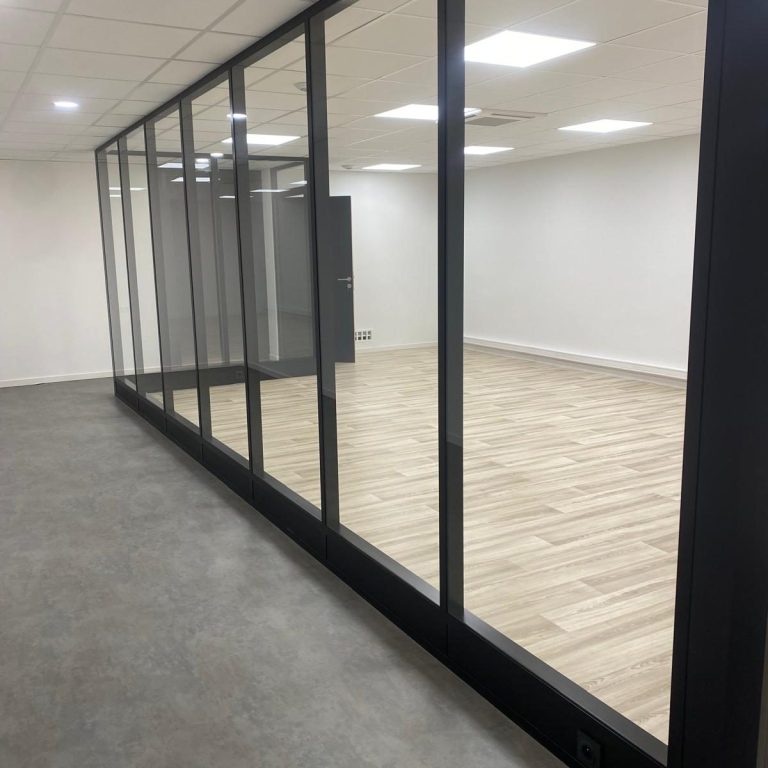 Bureau moderne avec des murs en verre, sol en bois et éclairage clair.