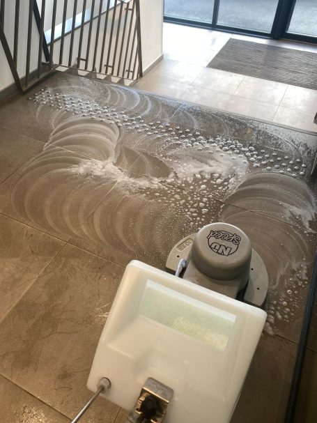 Remise en état sol d'une copropriété Sol en cours de nettoyage avec des traces d'eau et des bulles de savon.