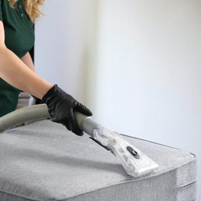 Une personne passe l'aspirateur sur un matelas gris.