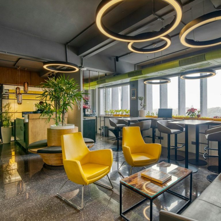 Intérieur moderne avec chaises jaunes, lumières circulaires et végétation, ambiance conviviale.