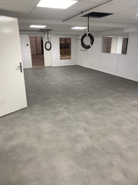 Remise en état site industriel Salle vide avec un sol gris, des murs blancs et deux anneaux suspendus au plafond.
