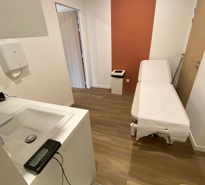 Salle d'examen médicale avec lit, lavabo et mur orange.