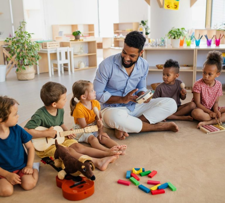 Un homme joue de la musique avec des enfants entourés de jouets colorés.