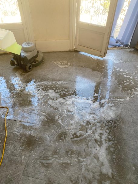 Nettoyage mécanisé du sol à la monobrosse Sol en béton humide avec traces de nettoyage et un aspirateur à côté.