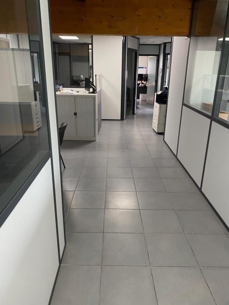 Couloir d'un bureau avec des fenêtres et des portes donnant sur des espaces de travail.