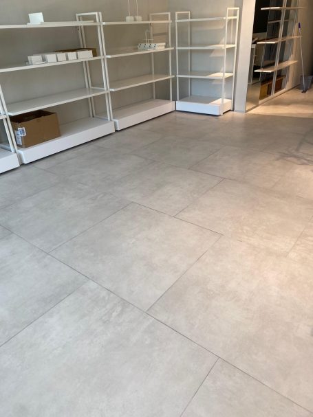Nettoyage après chantier d'un commerce Sol en carrelage clair avec des étagères blanches vides en arrière-plan.