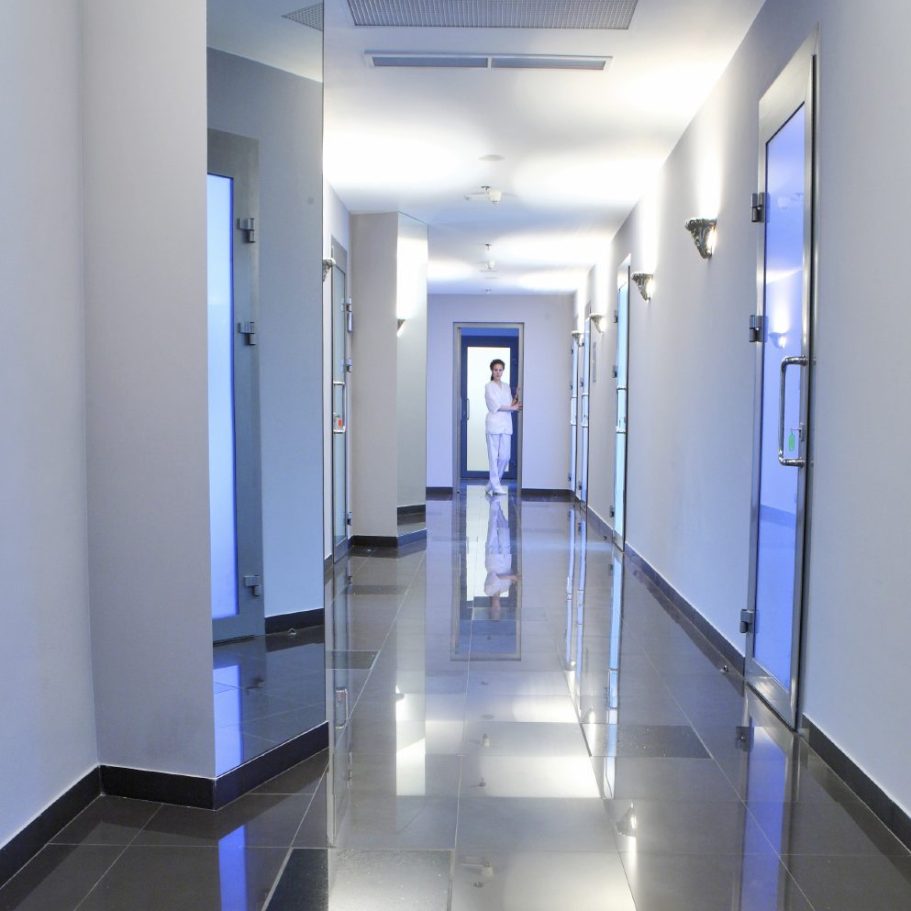 Un long couloir moderne avec un sol en marbre et des murs clairs. Des portes sont visibles.